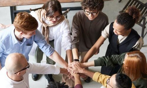 Group of young adults putting hands together in teamwork